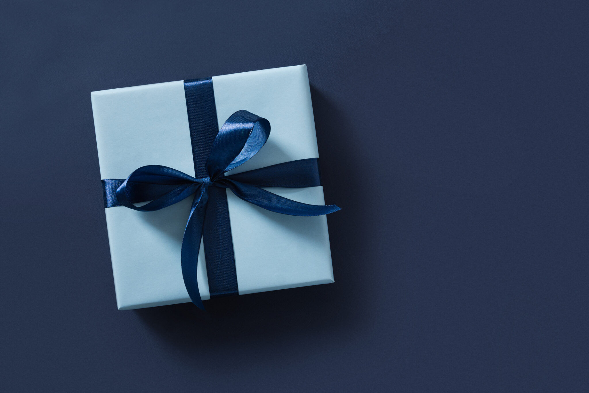 Blue gift box on navy blue background. View from above.